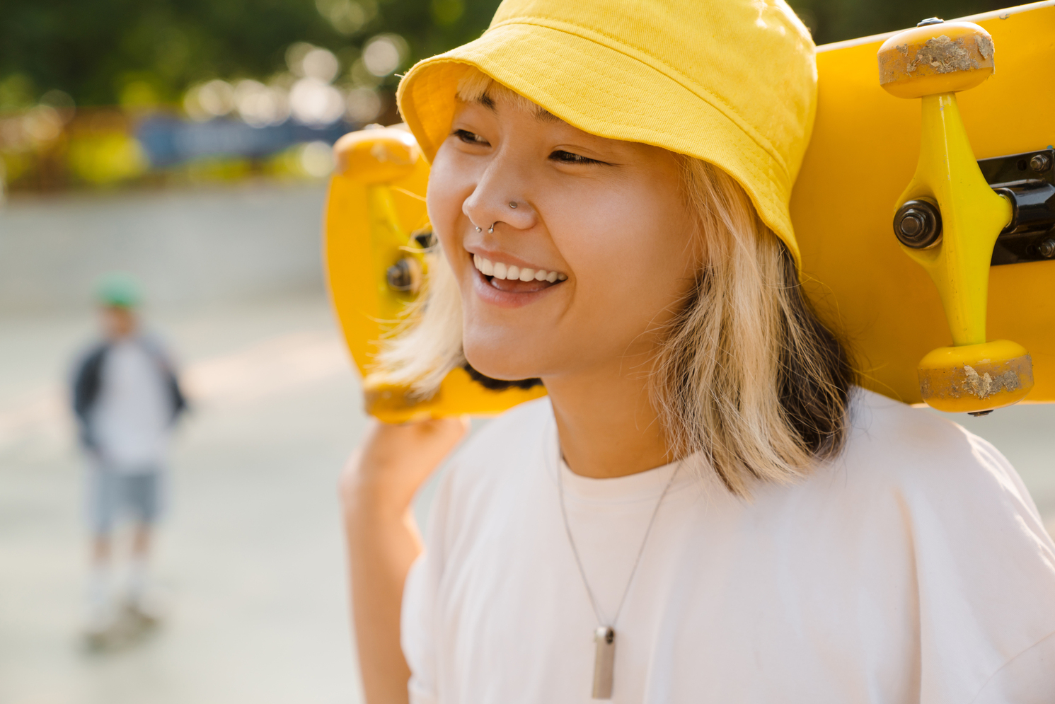 Asian girl wearing hat holding skateboard while laughing outdoors