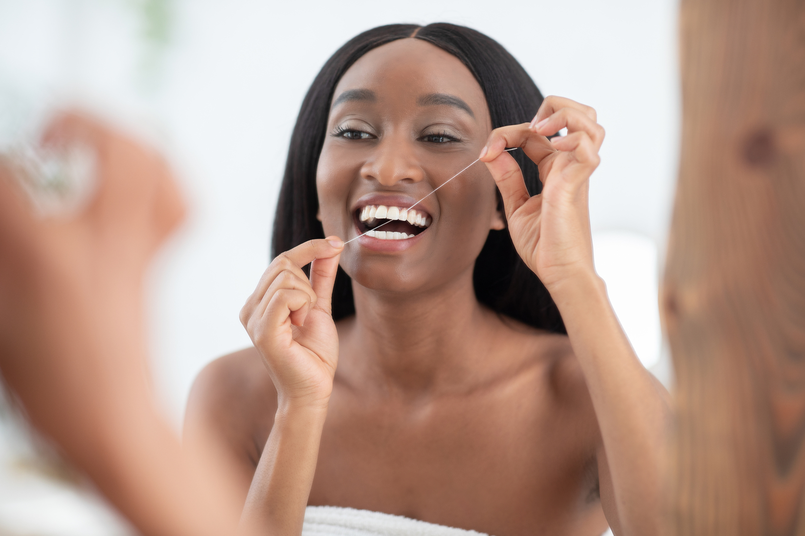 Dentistry at home, snow-white smile and oral care. Cheerful young african american woman brushes her teeth with dental floss and looks in mirror in interior of bedroom in morning, close up, copy space
